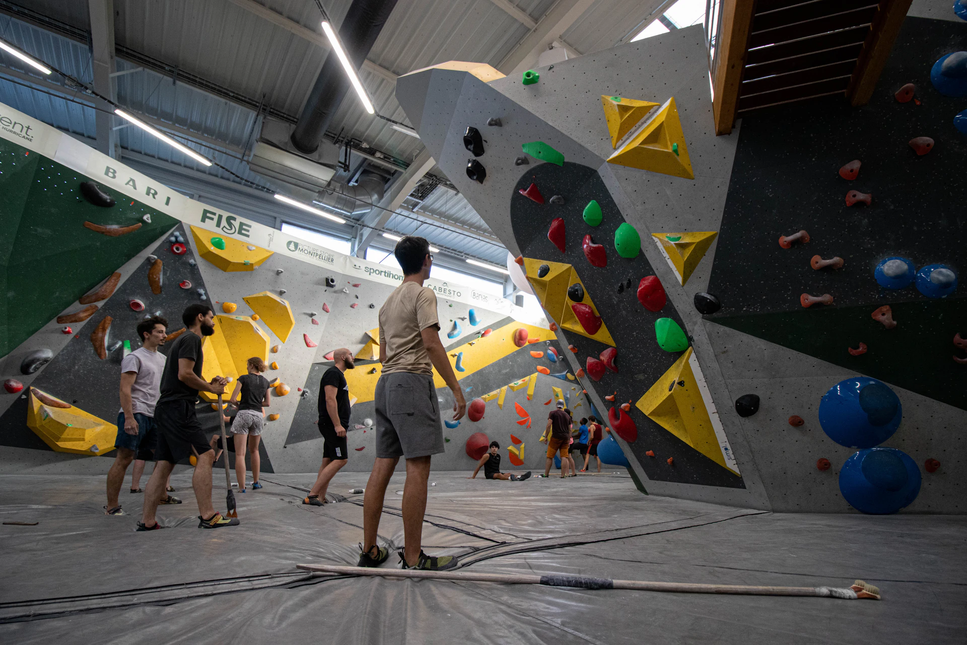Climbers moving across a bright indoor bouldering wall covered in colorful holds at Sender