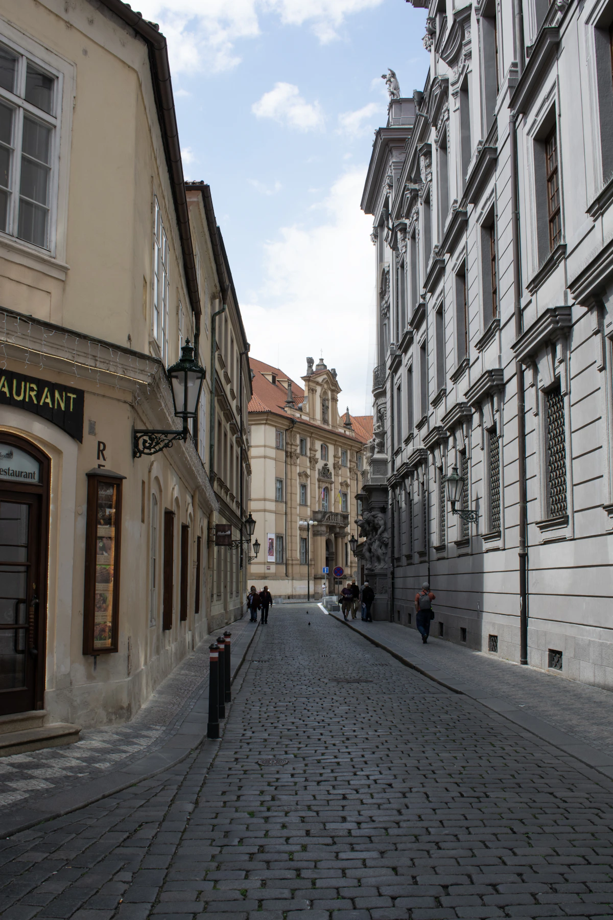 A quiet cobbled lane curving between historic buildings in Prague