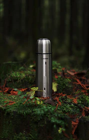A stainless steel water bottle sitting on top of a moss covered forest