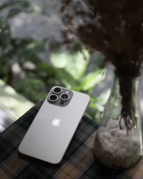 A cell phone sitting on top of a table next to a vase filled with flowers