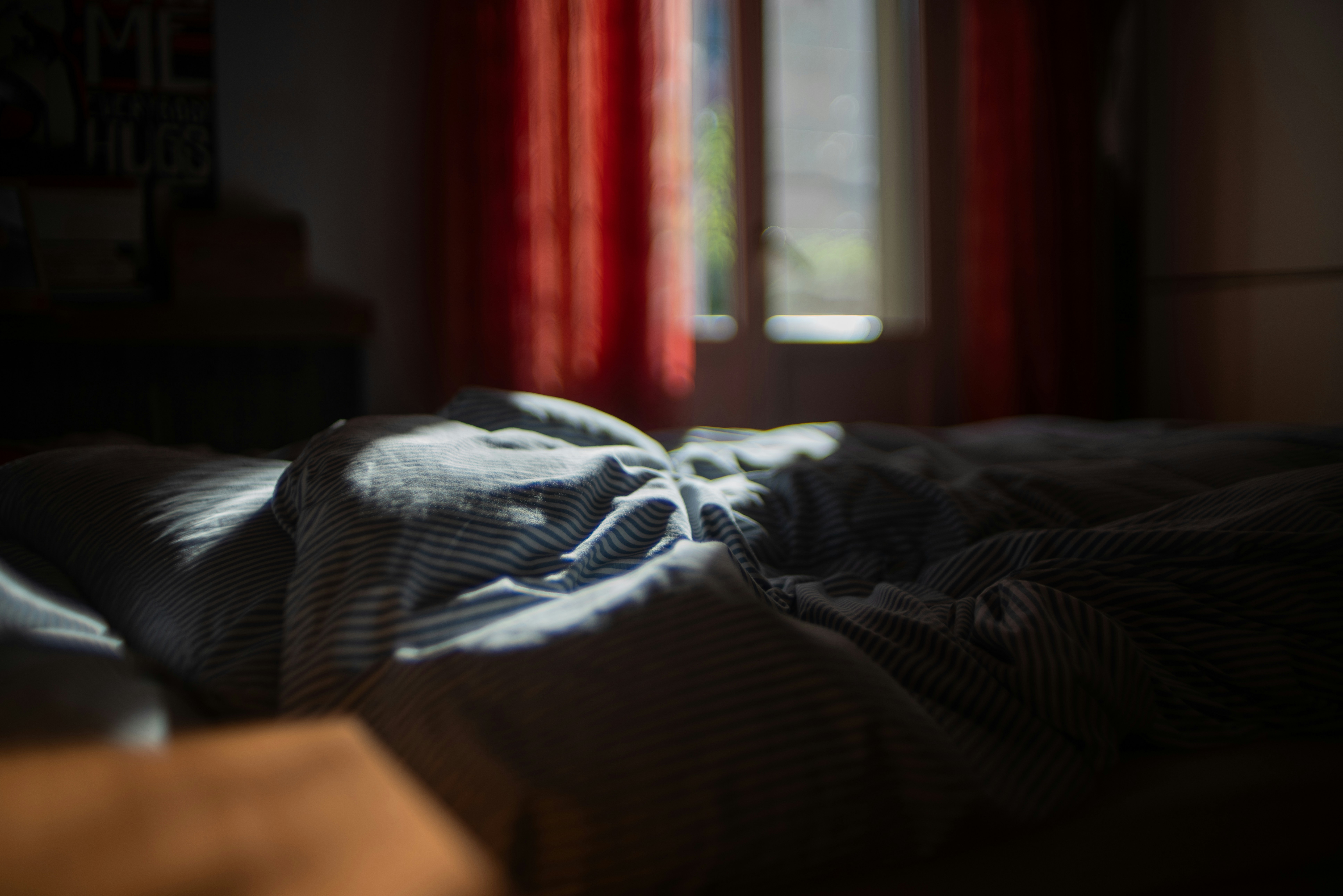 An unmade bed in a dark room with red curtains