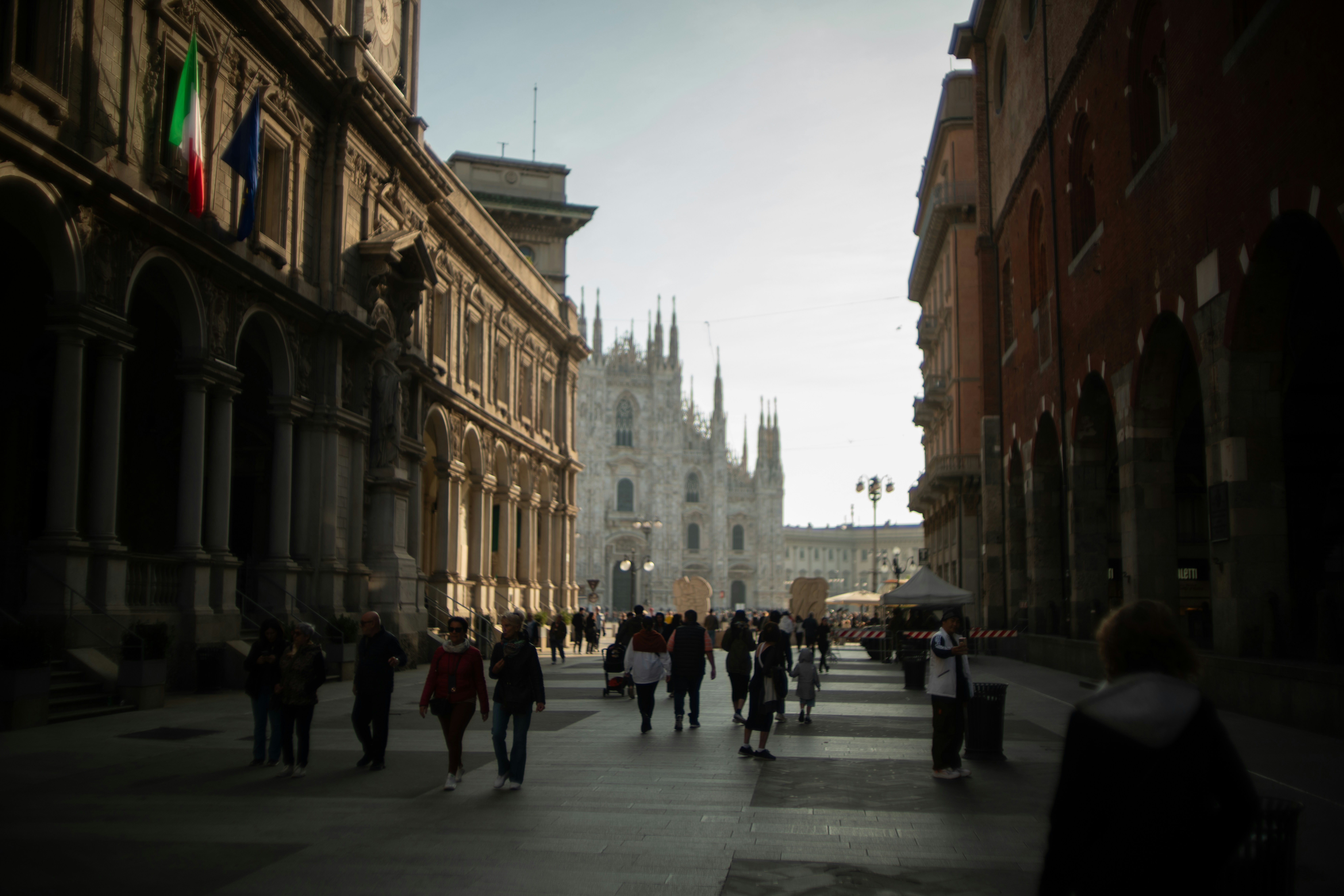 A group of people walking down a street next to tall buildings