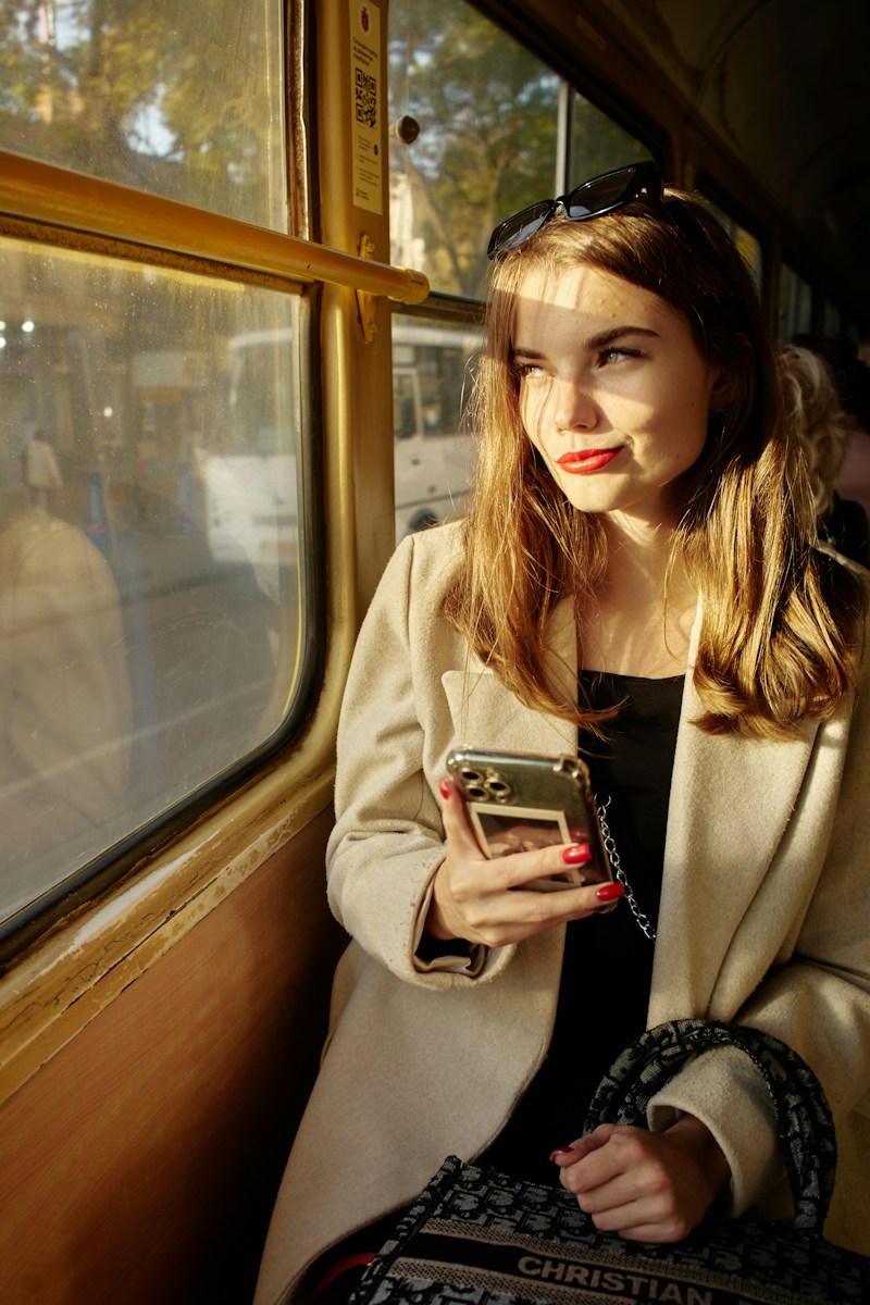 Woman in a camel coat on a train looking at her phone, placeholder editorial image