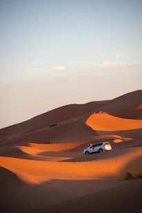 A car driving through the desert with sand dunes in the background