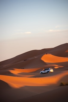 A car driving through the desert with sand dunes in the background
