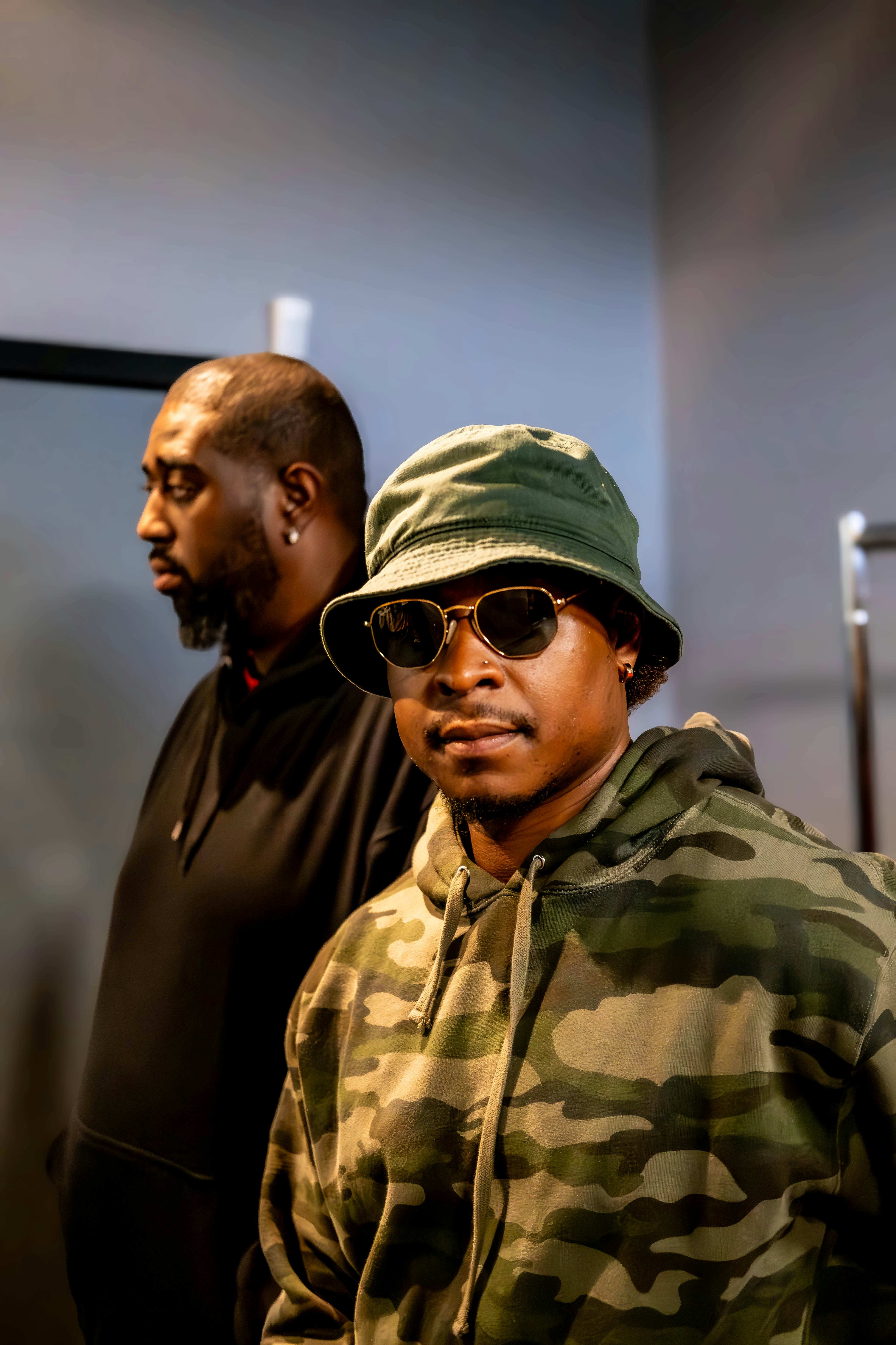 A man in a camouflage jacket and hat standing next to another man