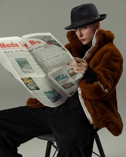 A woman sitting on a stool reading a newspaper