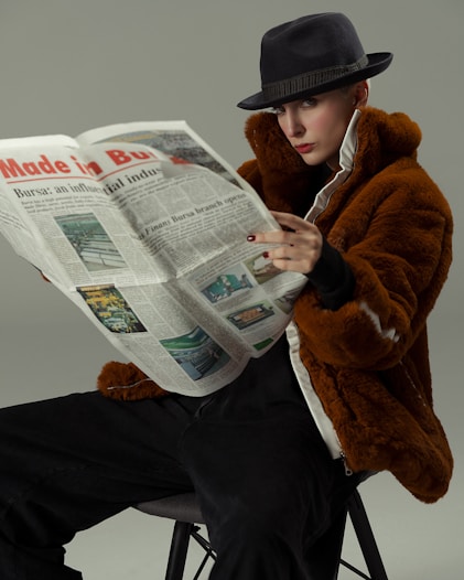 A woman sitting on a stool reading a newspaper