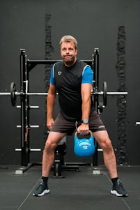 A man squats with a blue kettle in a gym