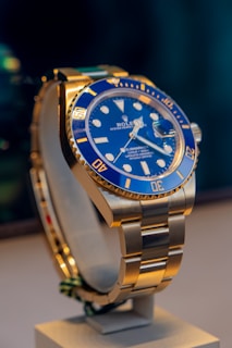 A blue and gold rolex watch on a stand