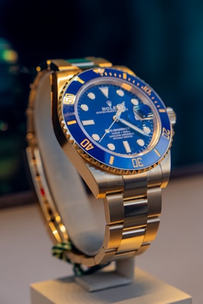 A blue and gold rolex watch on a stand