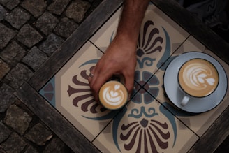A person holding a cup of coffee on top of a tiled floor