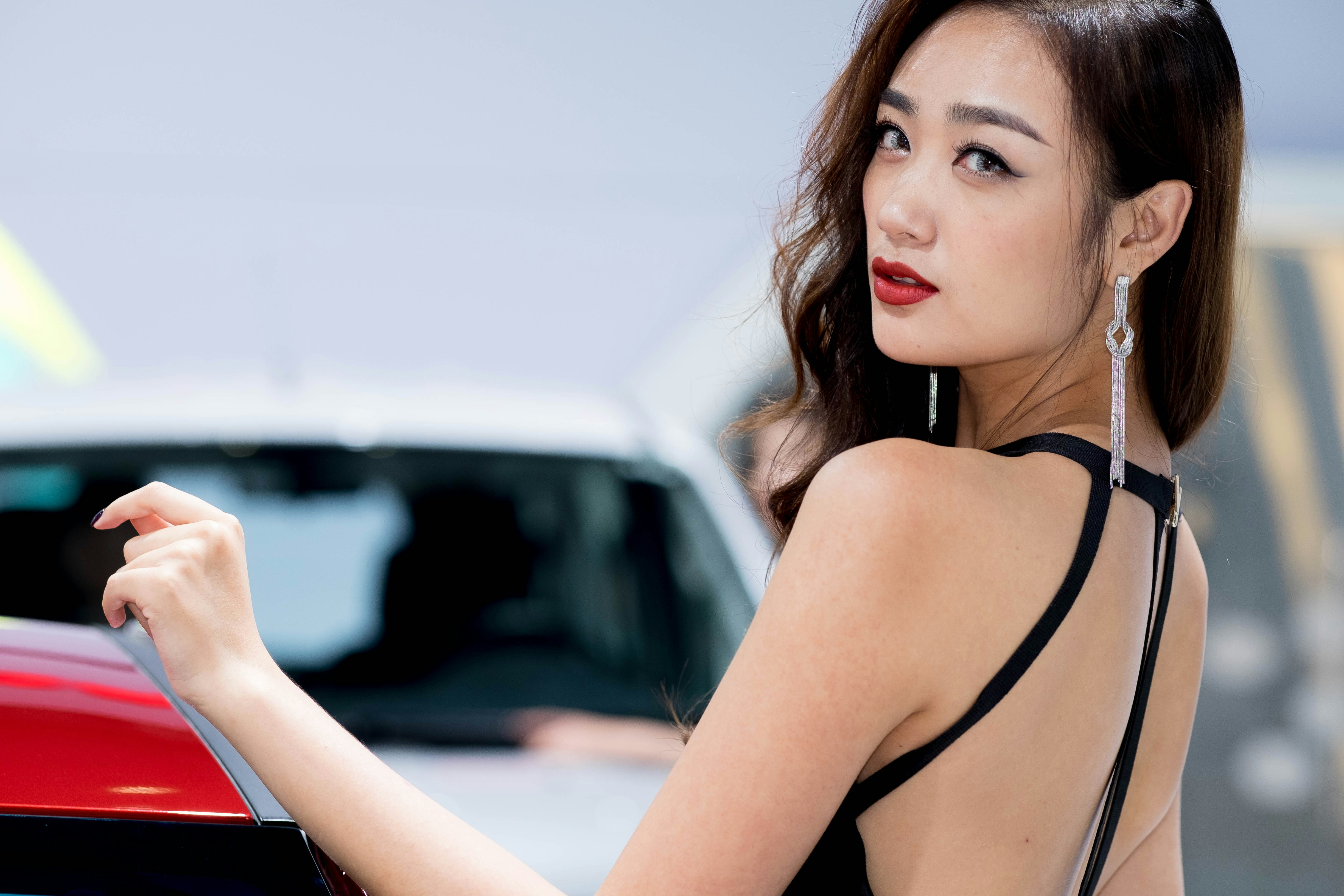 A woman in a black dress standing next to a red car