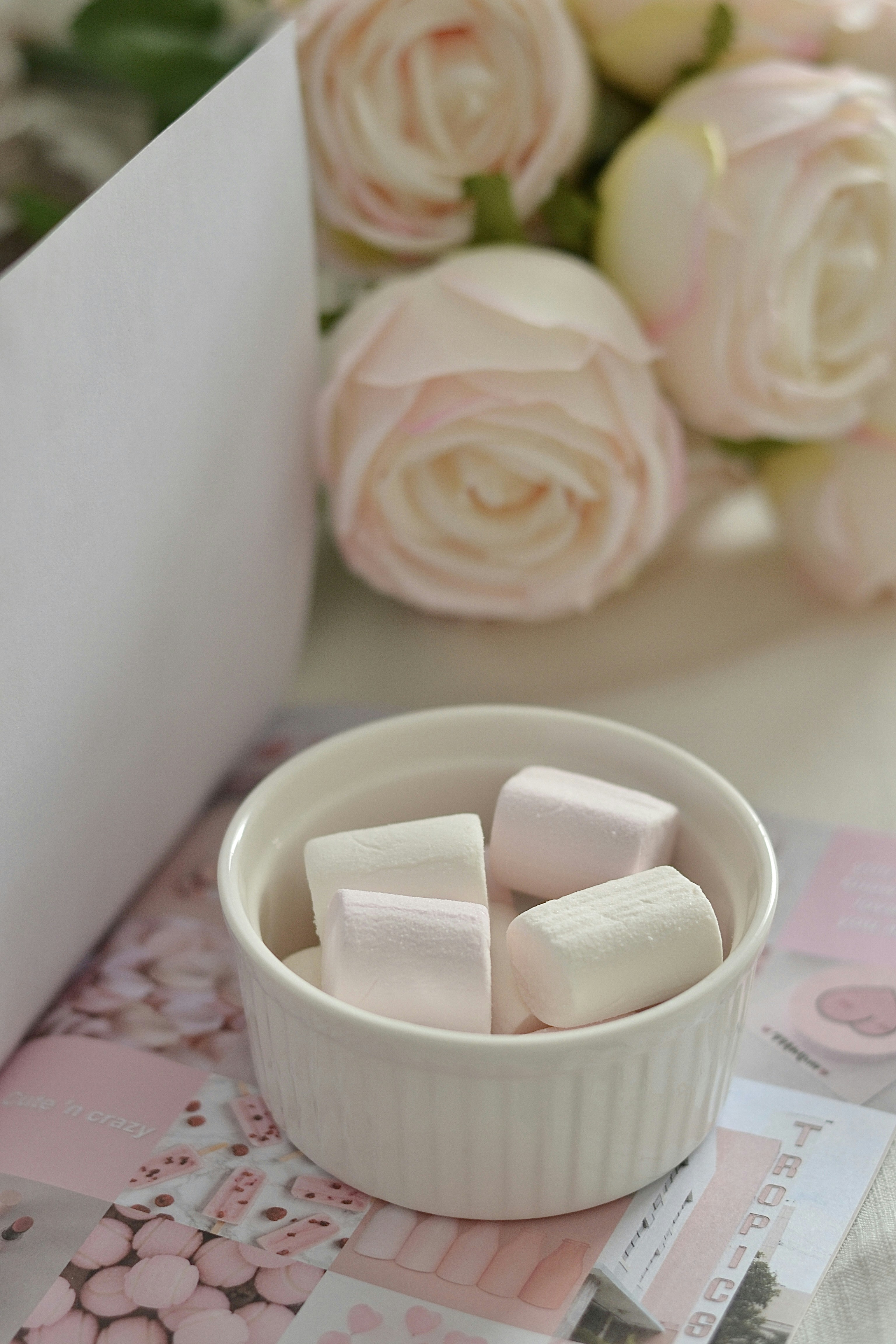 A white bowl filled with marshmallows next to a bouquet of roses