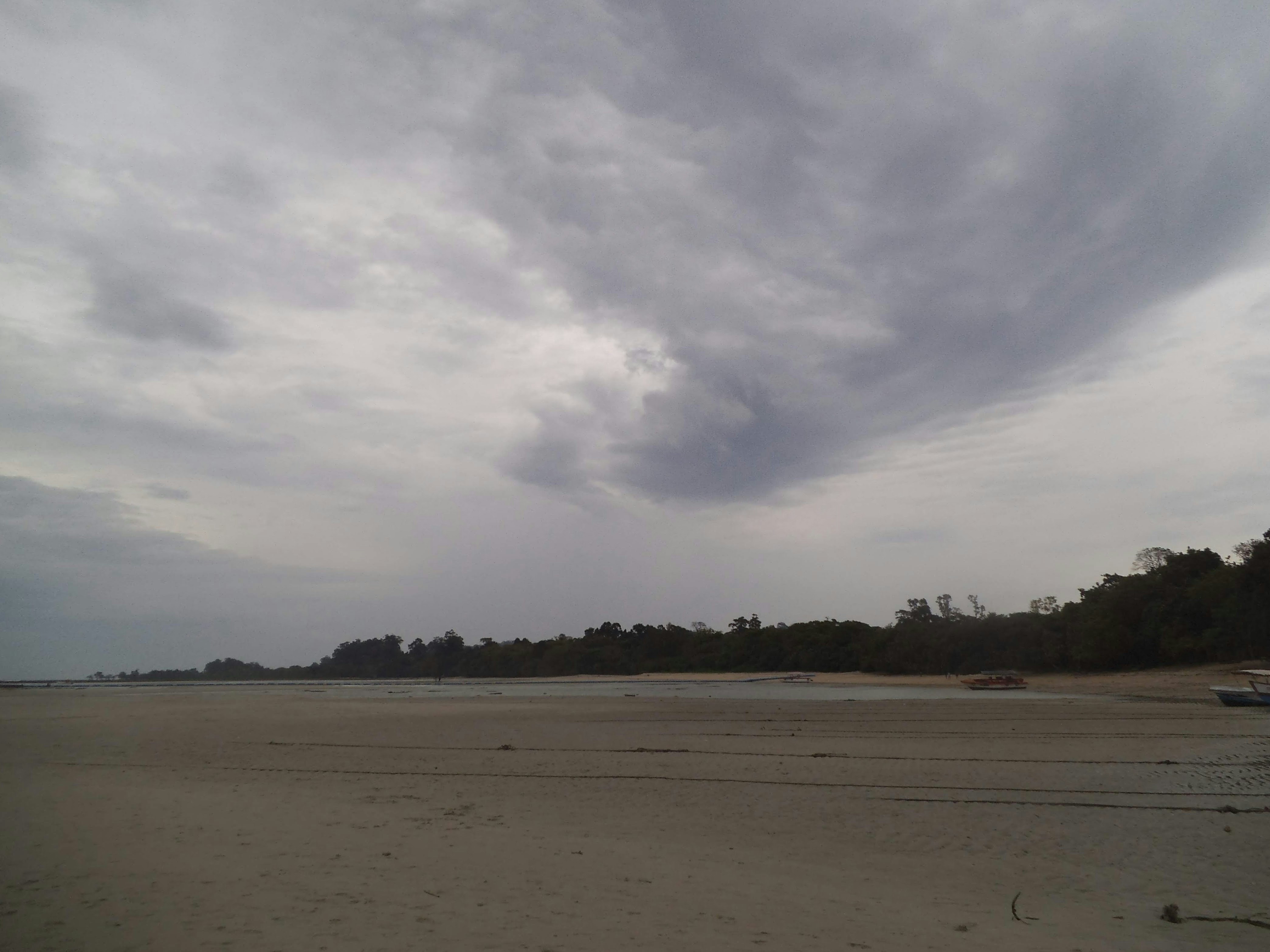 A cloudy sky over a beach with a boat in the water