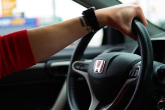 A woman is driving a car with her hand on the steering wheel
