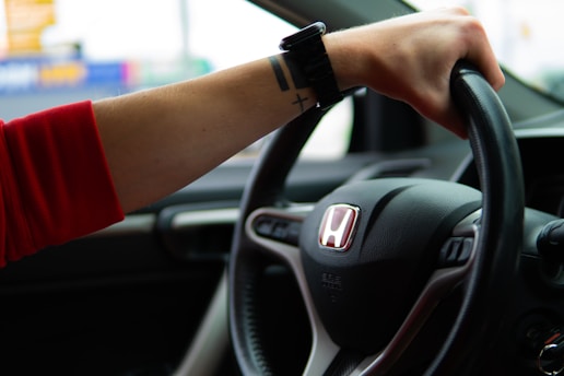 A woman is driving a car with her hand on the steering wheel