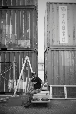 A man sitting on top of a car in front of shipping containers