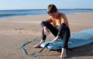 A boy sitting on a surfboard on the beach in new hampshire