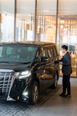A man in a suit standing next to a black car