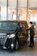 A man in a suit standing next to a black car