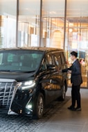 A man in a suit standing next to a black car