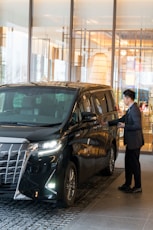 A man in a suit standing next to a black car