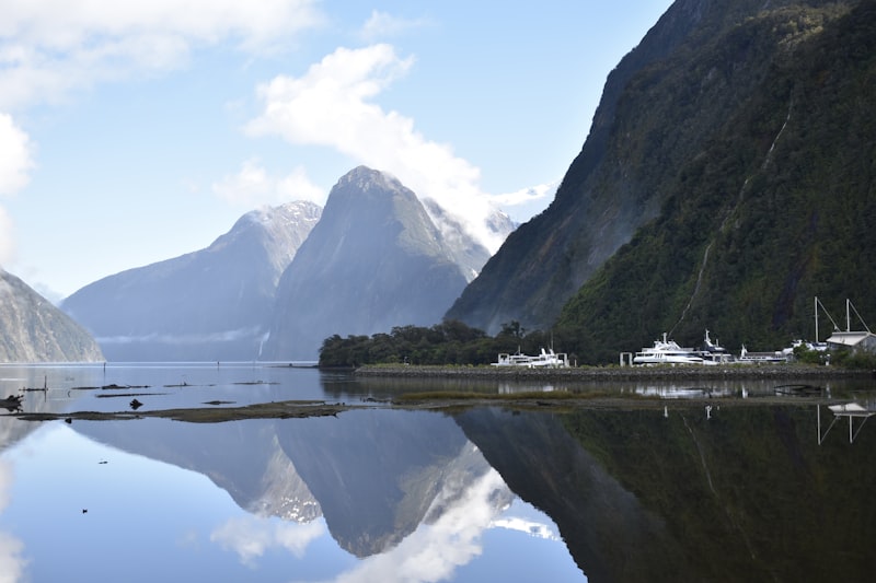 Mitre Peak and steep fiord walls mirrored in the glassy water of Milford Sound under drifting cloud