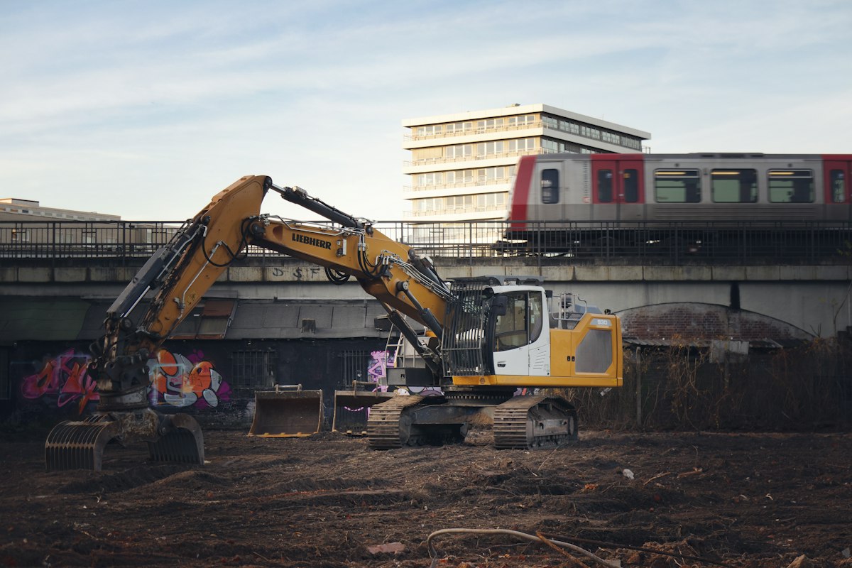Tracked excavator with a lowered bucket at an exposed urban earthwork site.