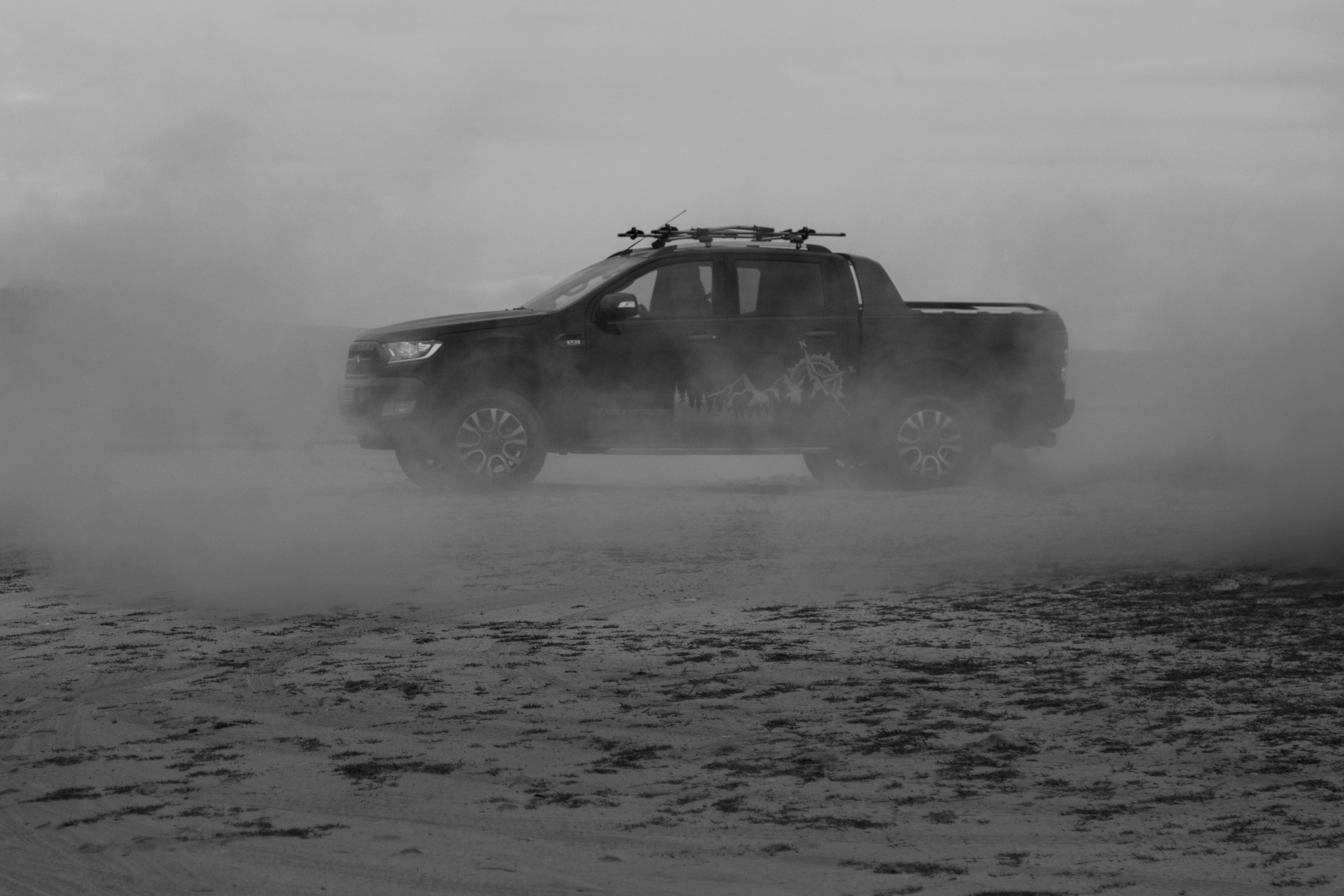 A black and white photo of a truck driving on a dirt road