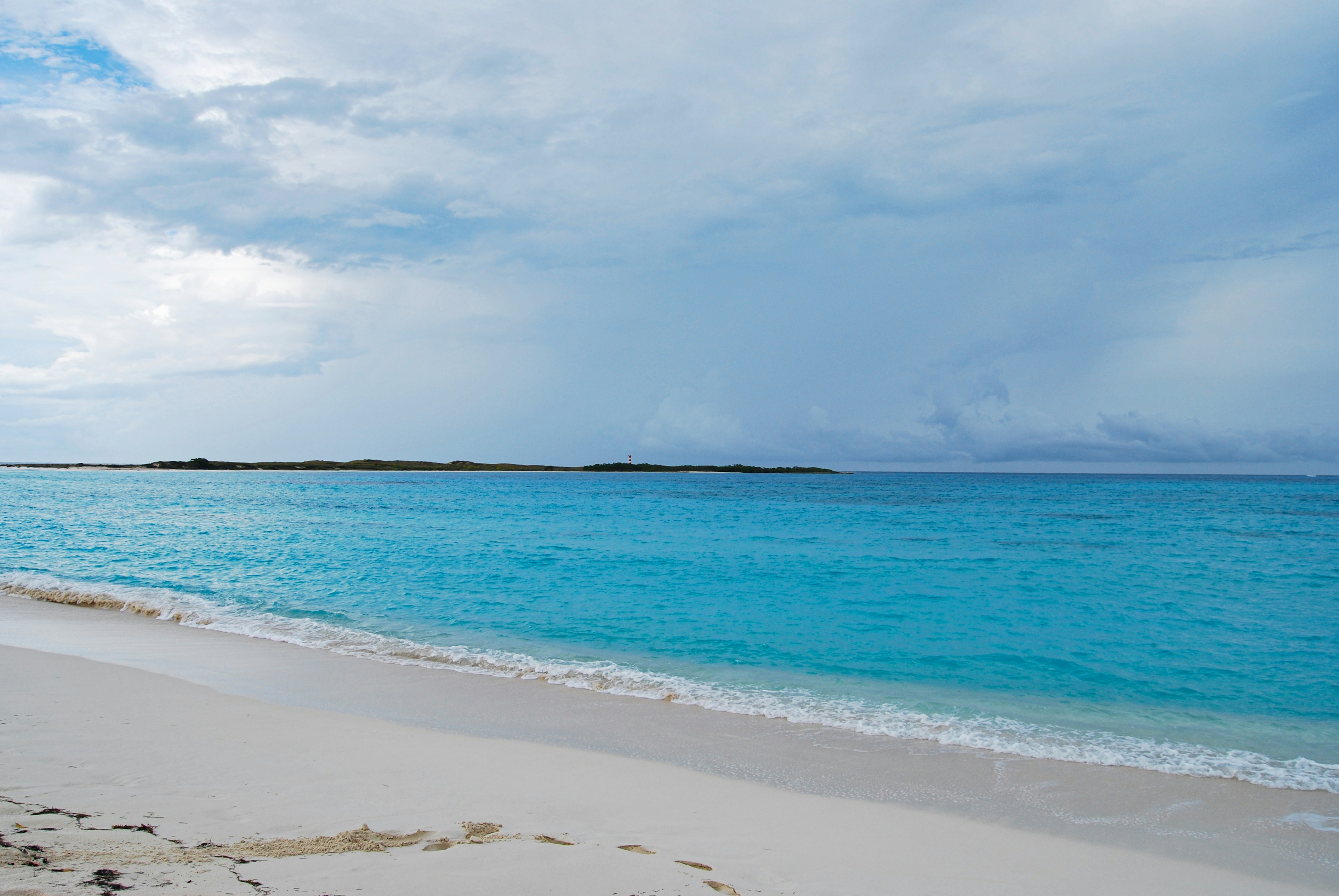 A sandy beach with blue water and clouds