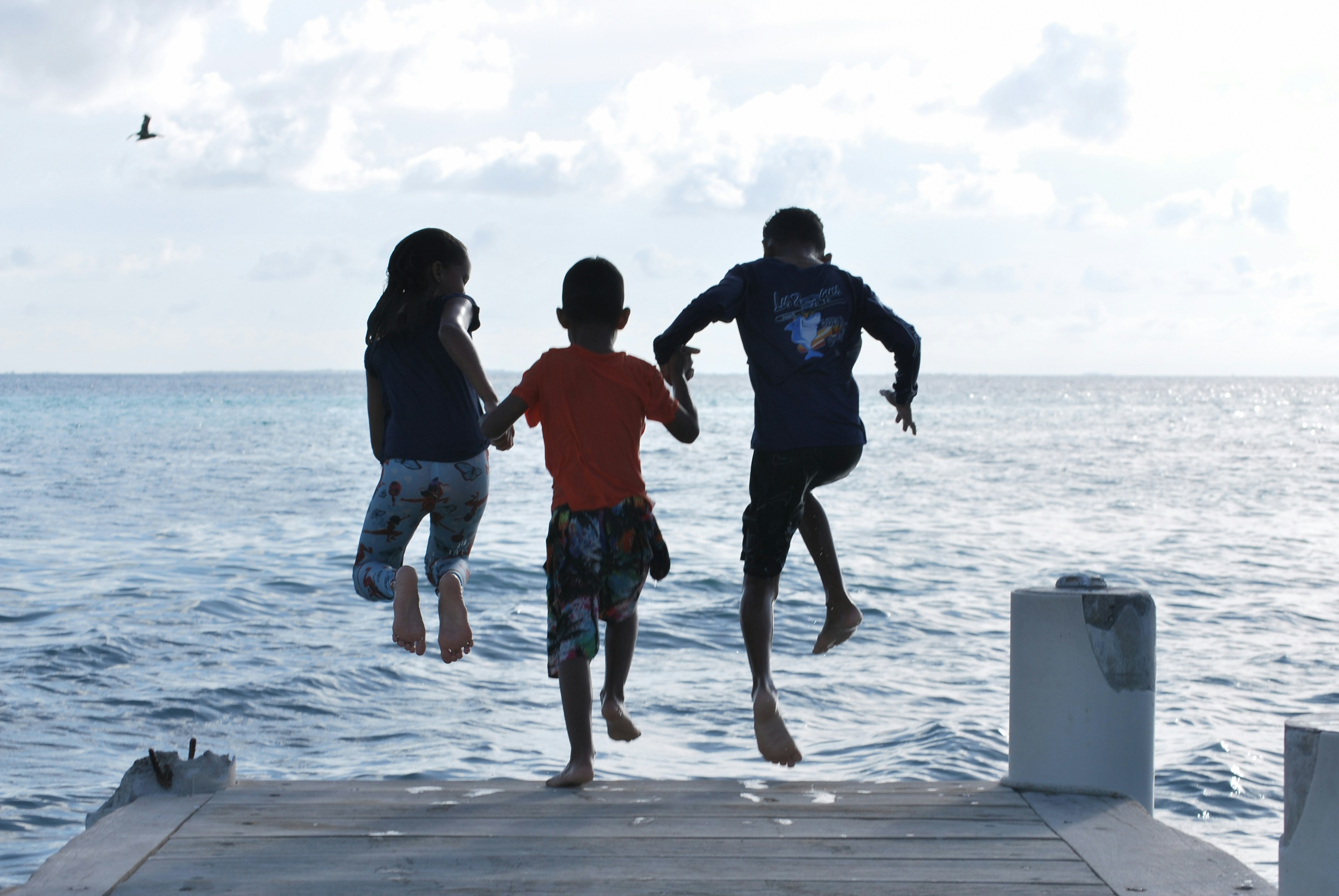 Three people jumping off a dock into the ocean