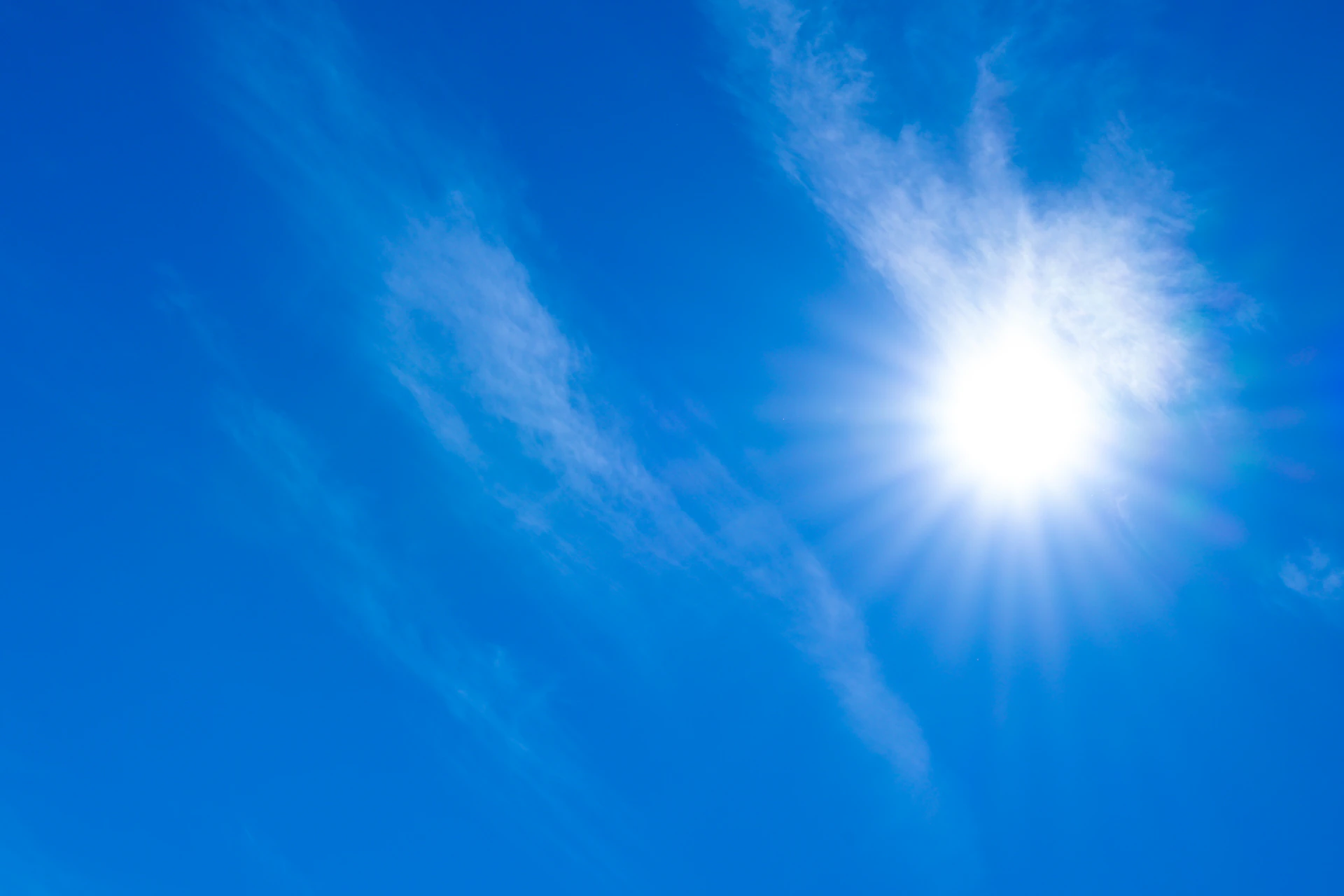 A bright blue sky with the sun shining through the clouds