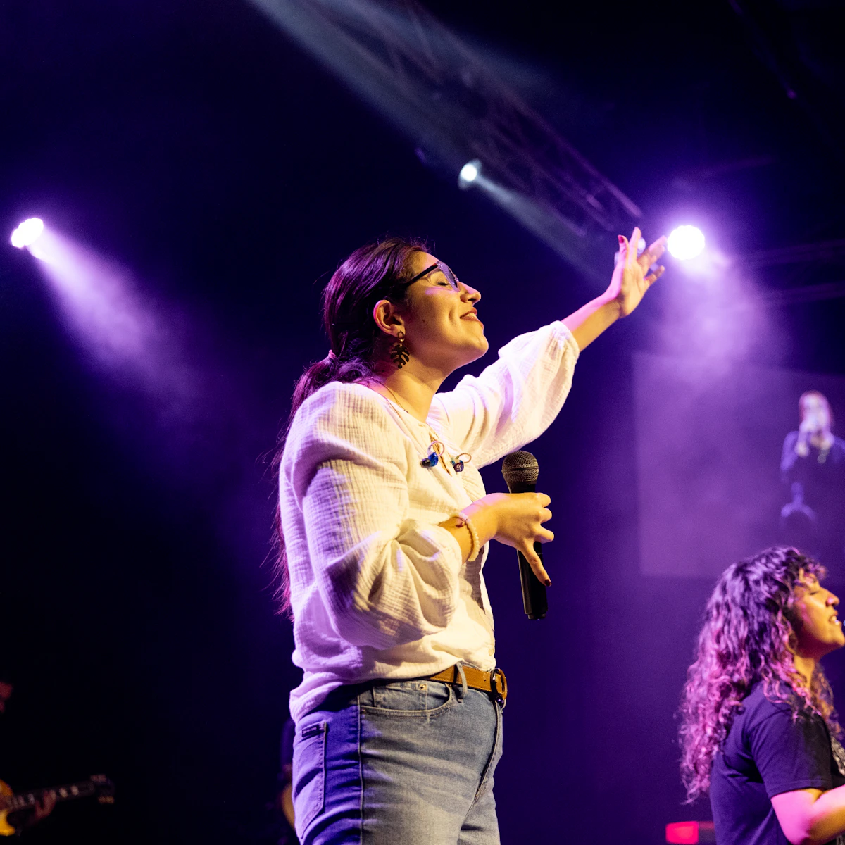 Worship leader singing on a stage lit with purple lights