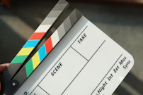 A person holding a movie clapper and a pair of scissors