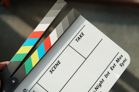 A person holding a movie clapper and a pair of scissors