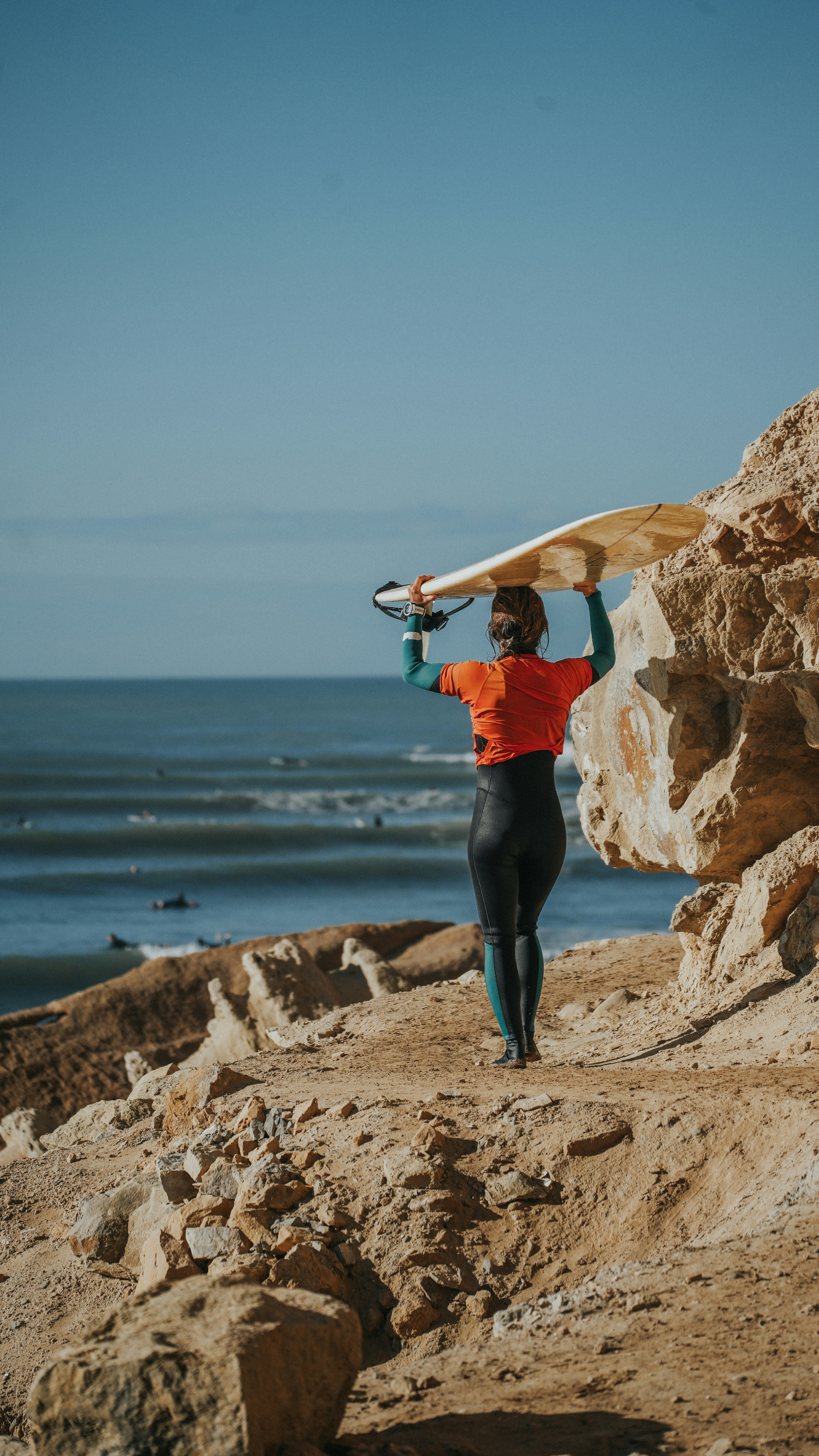 Un homme portant une planche de surf au sommet d’une plage rocheuse