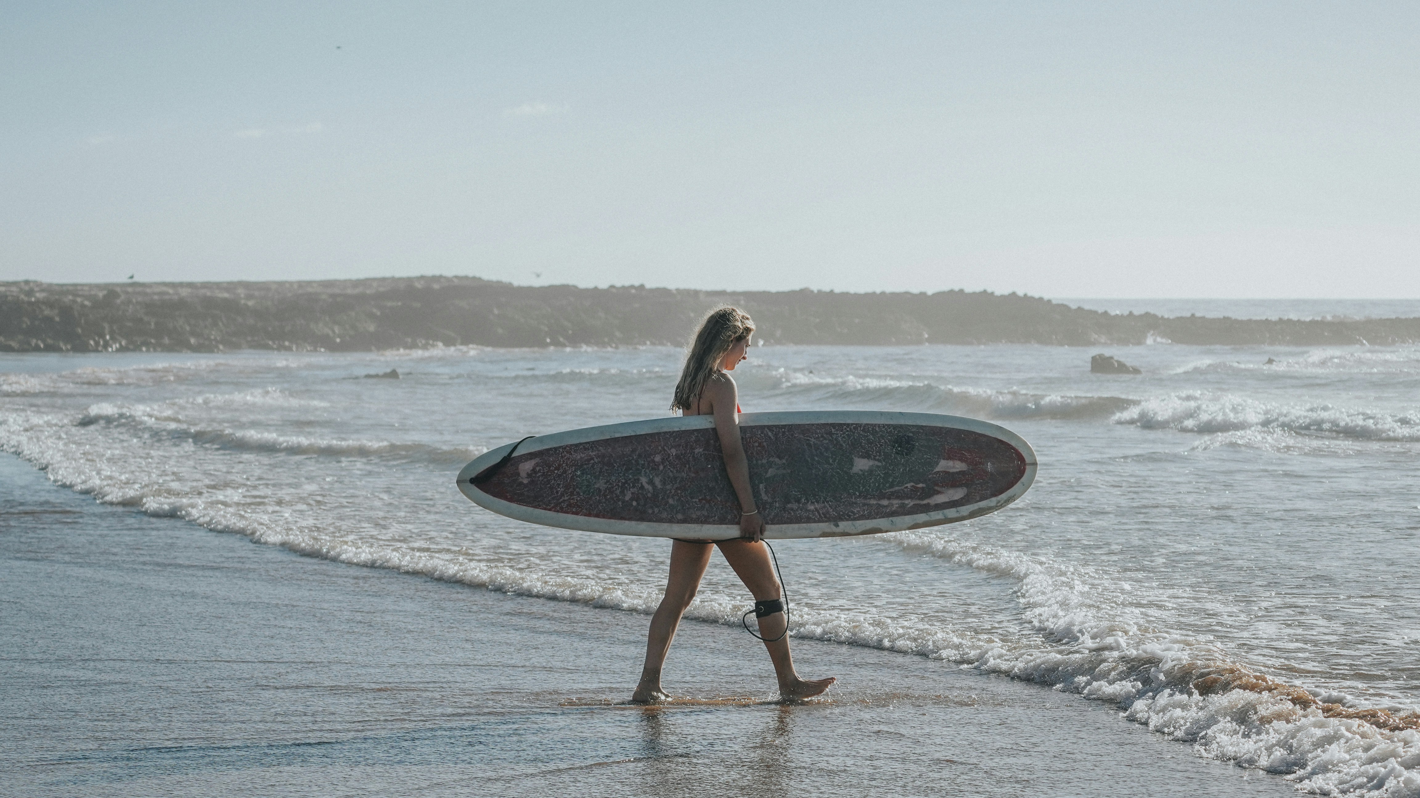 Une femme marchant sur la plage avec une planche de surf