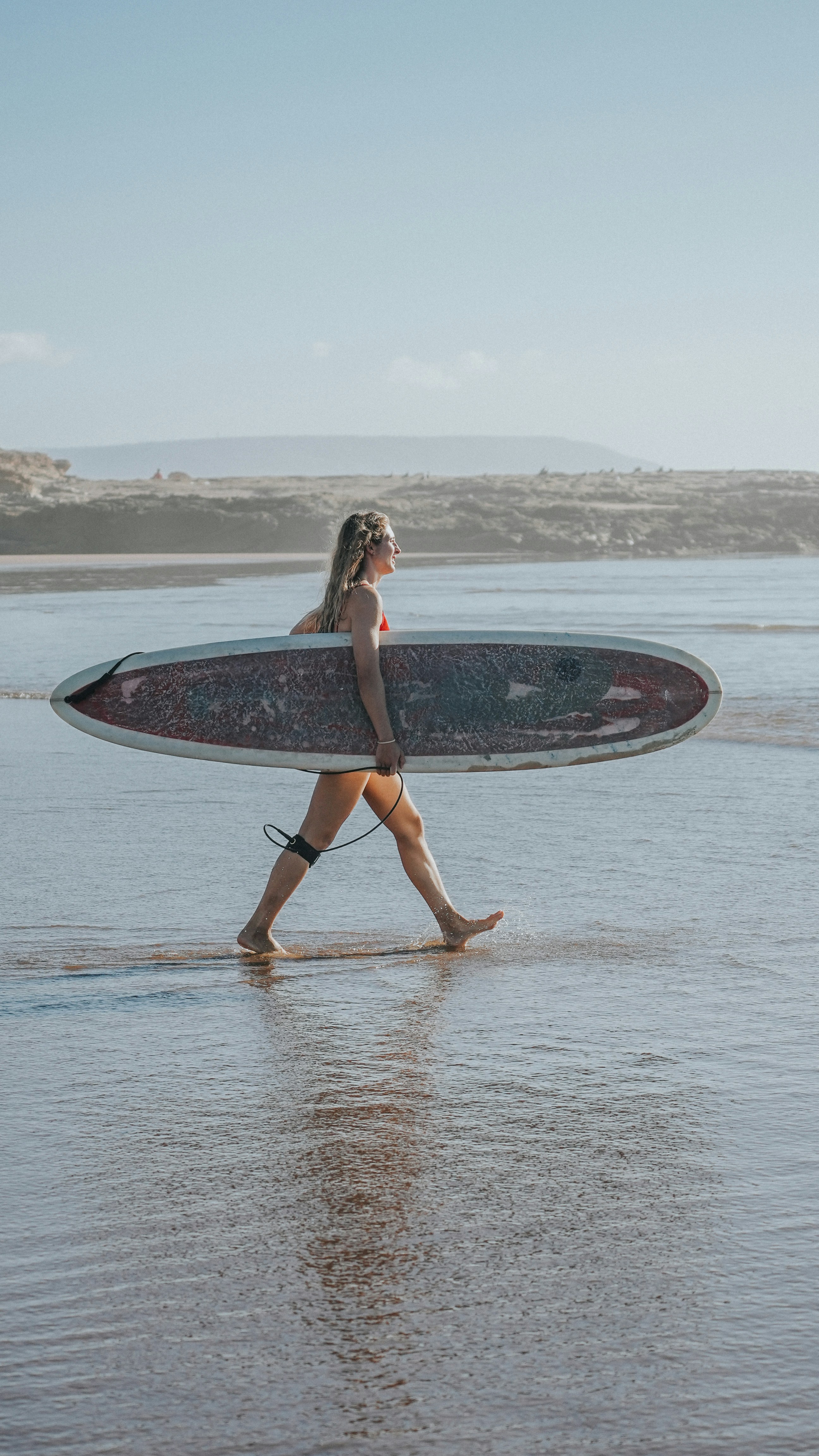 Une femme traversant une plage avec une planche de surf