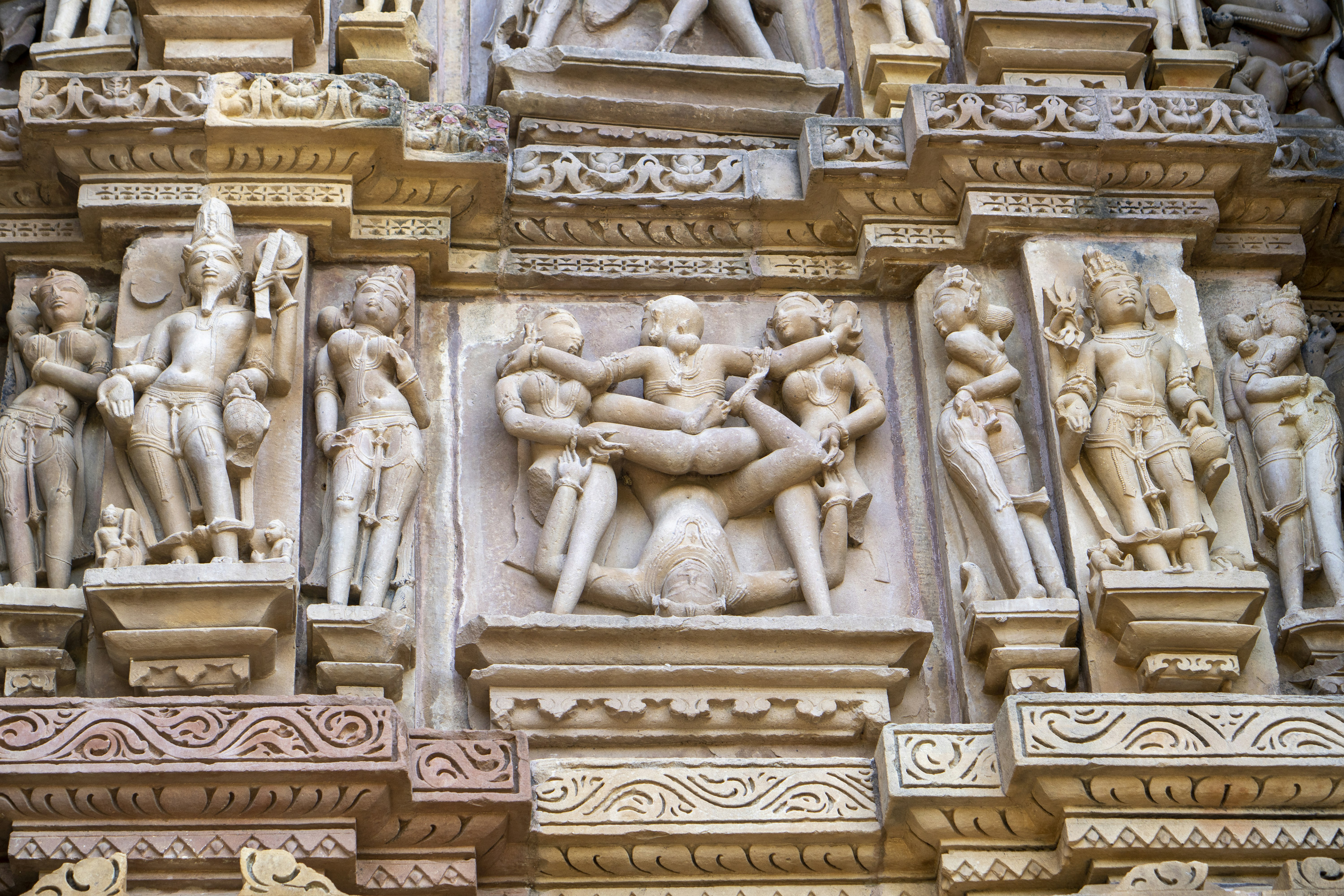 Intricate ancient stone carved temple reliefs showing figures and decorative motifs, dramatic raking light