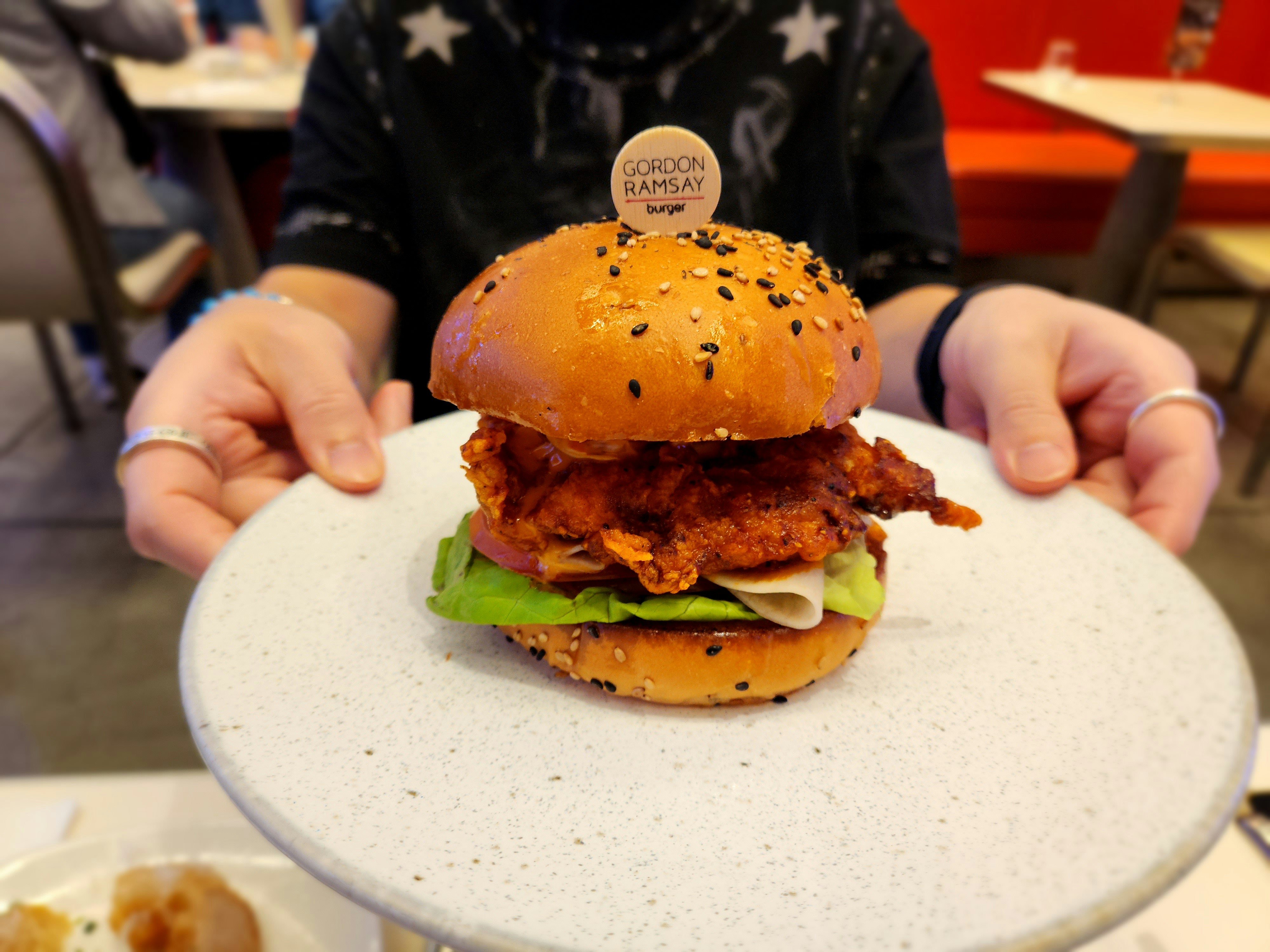 Hands presenting a fried chicken burger on a plate