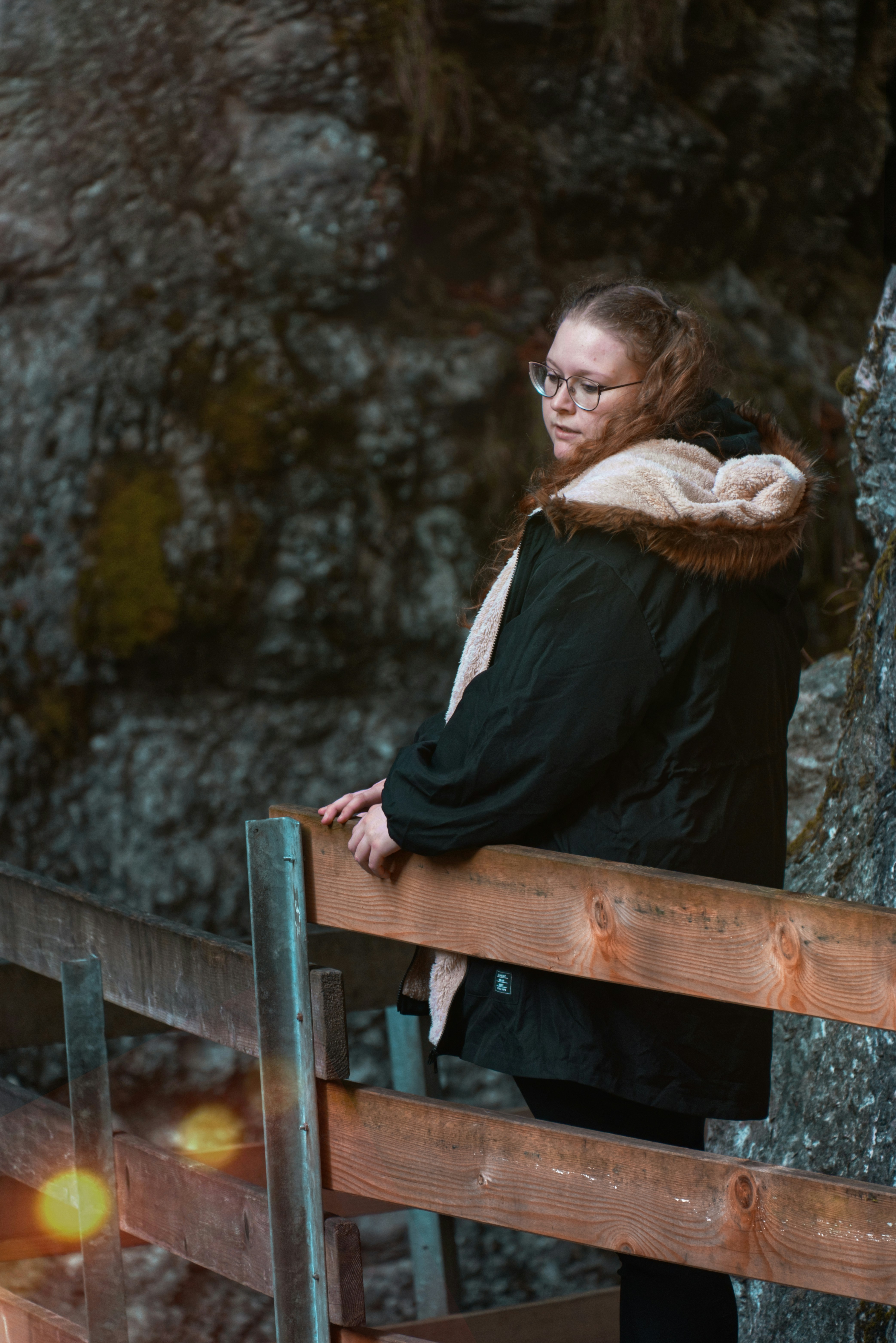 A woman standing on a wooden fence next to a tree