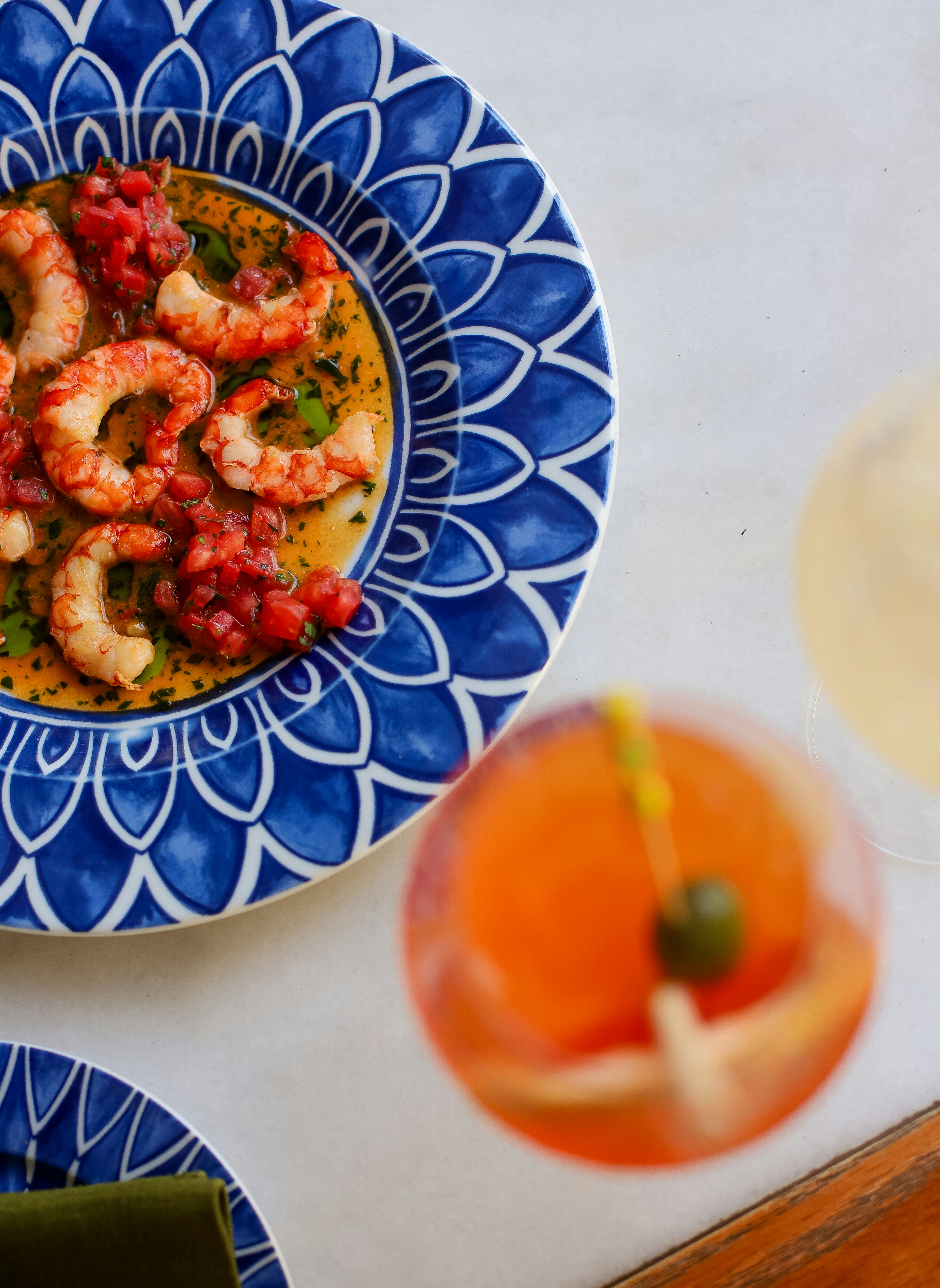 A blue and white plate topped with shrimp next to a glass of orange juice