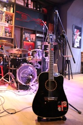 A black guitar sitting on top of a hard wood floor