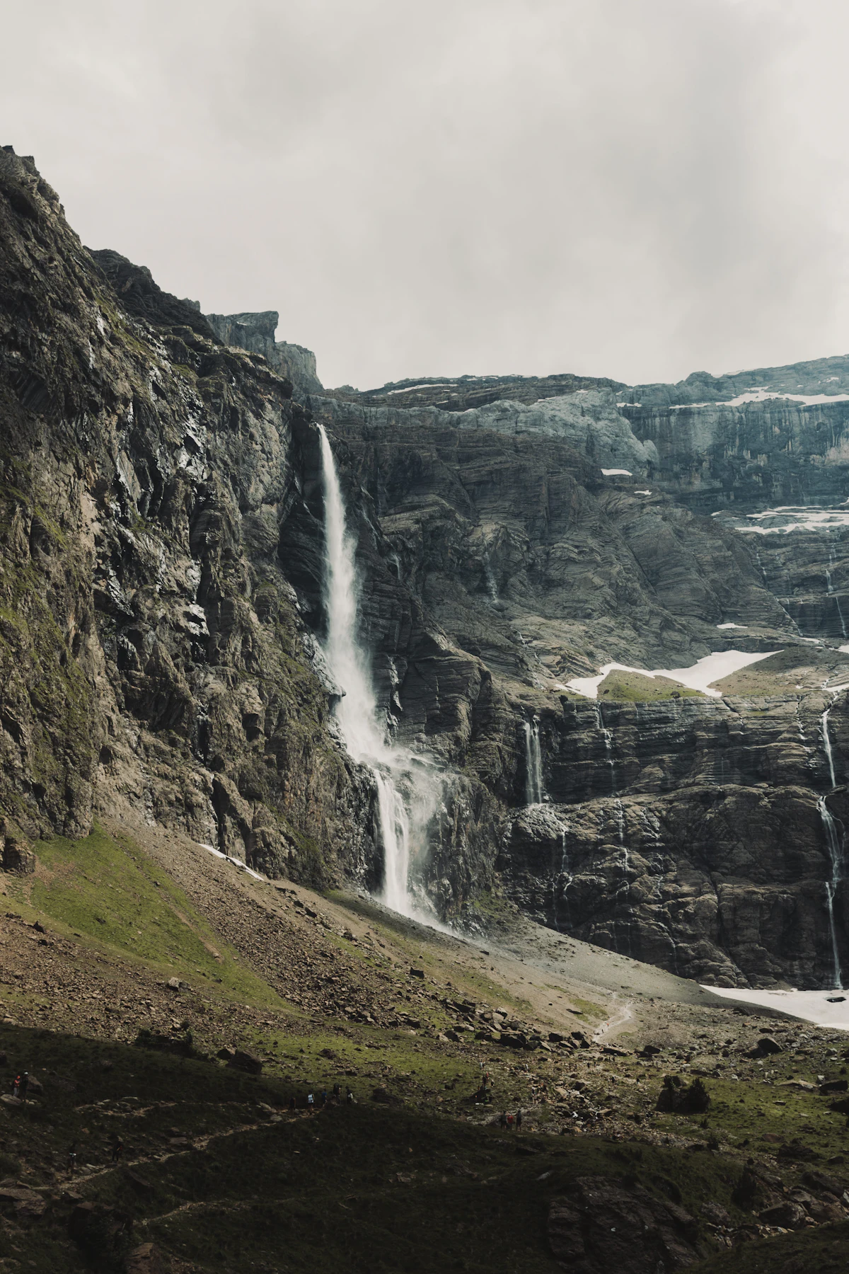 A tall waterfall pouring down the rock walls of the cirque de Gavarnie, with snow patches at the foot