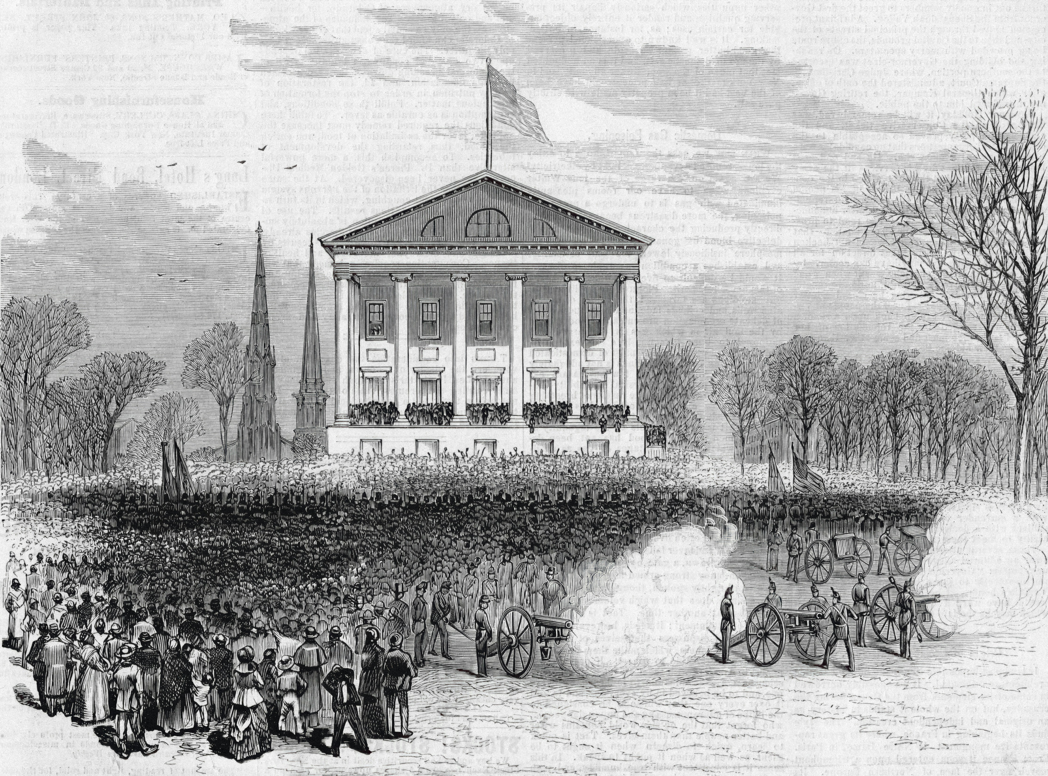 A large crowd gathers before a grand building with columns.