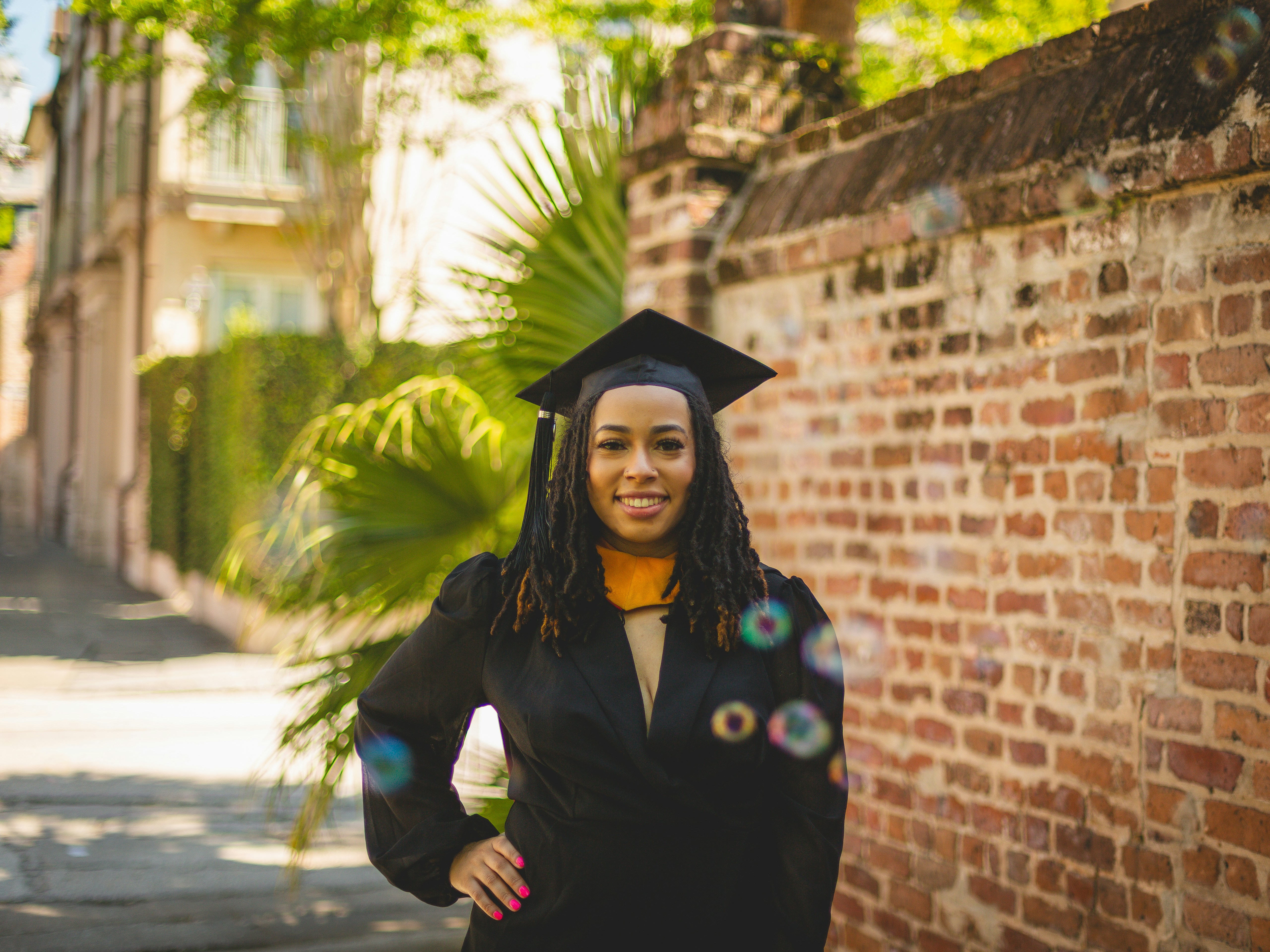 A woman in a graduation cap and gown standing in front of a brick wall