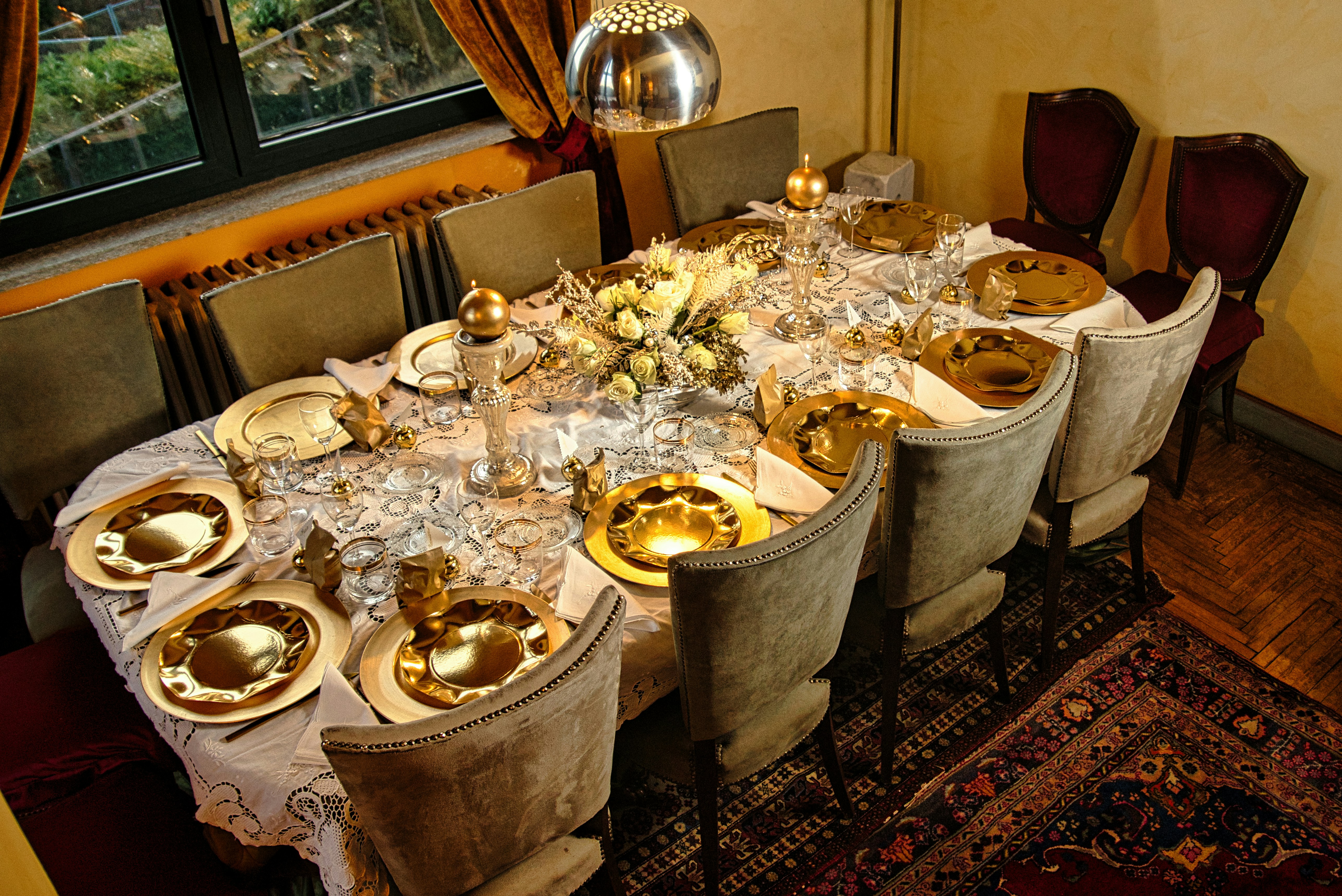 A dining room table is set with gold plates and silverware, a collection of glasses, cake stands, decorations and tablecloths for beautiful laid tables