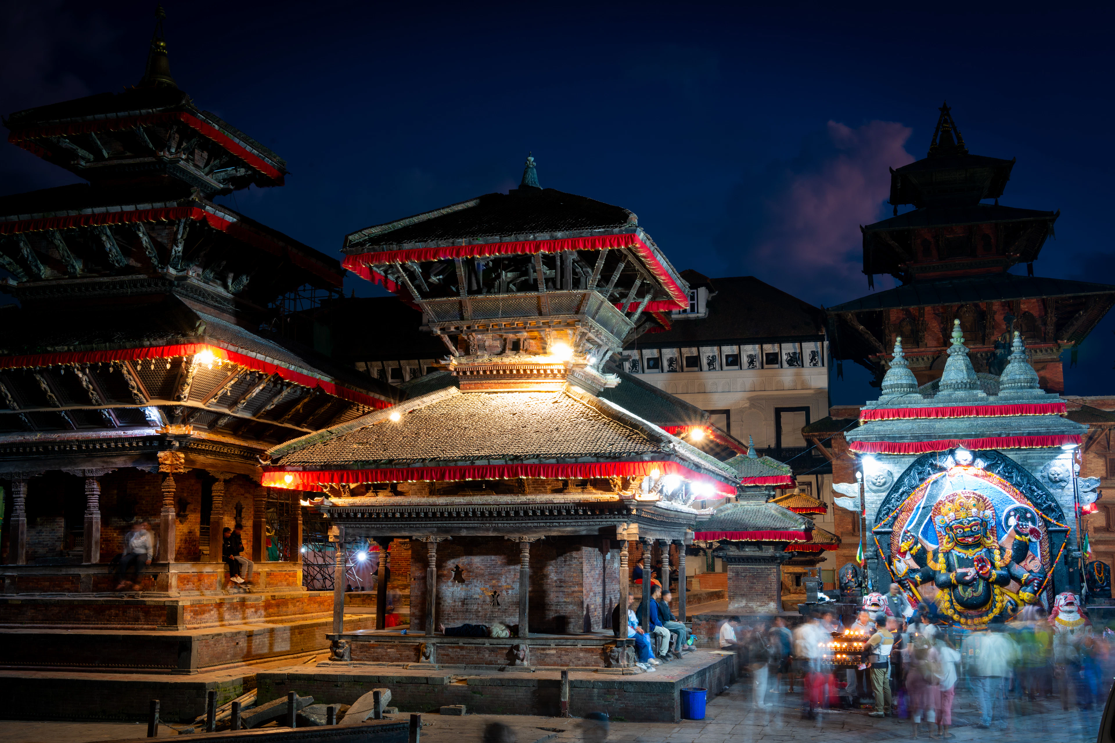 Illuminated red pagoda temples glow at night around a shrine in Kathmandu Durbar Square.