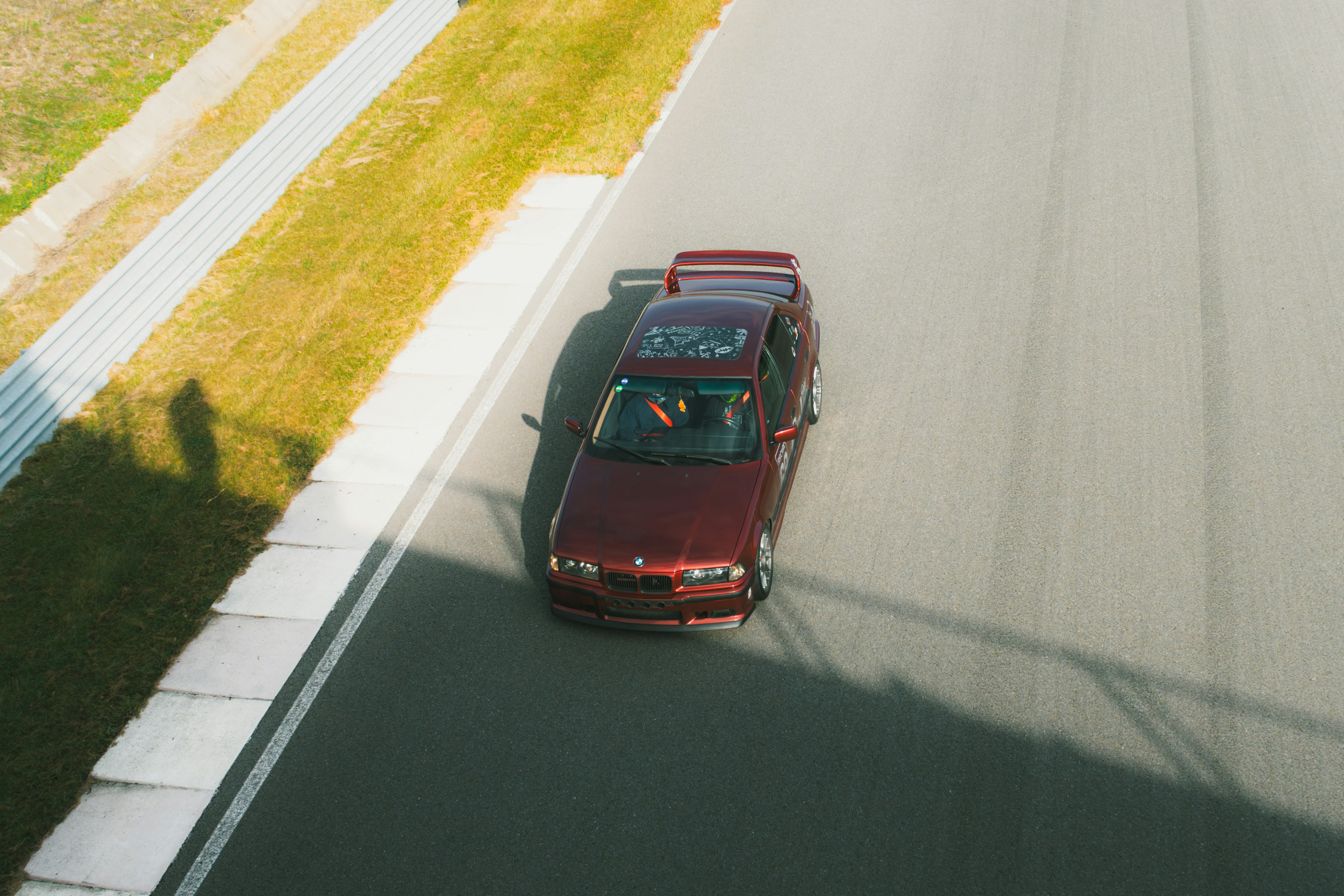 A red car driving down a road next to a lush green field
